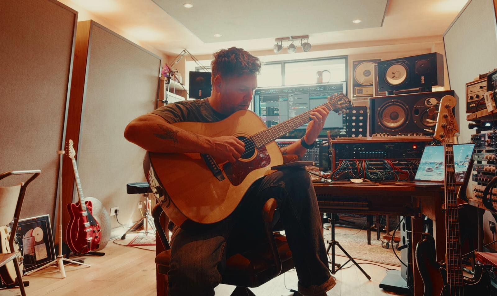 Playing acoustic guitar in the studio, surrounded by monitors and outboard gear